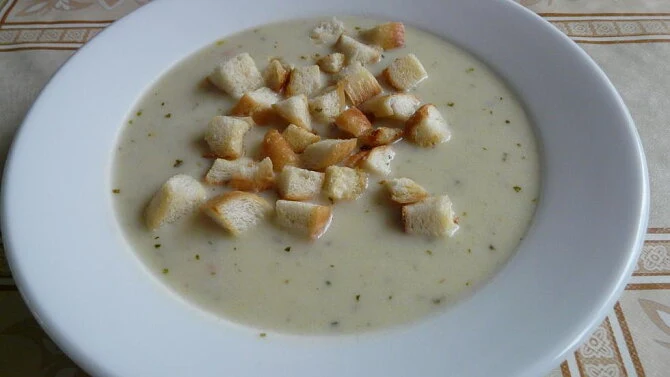 Kremová polévka s chlebíčky v bílé misce na stolu.