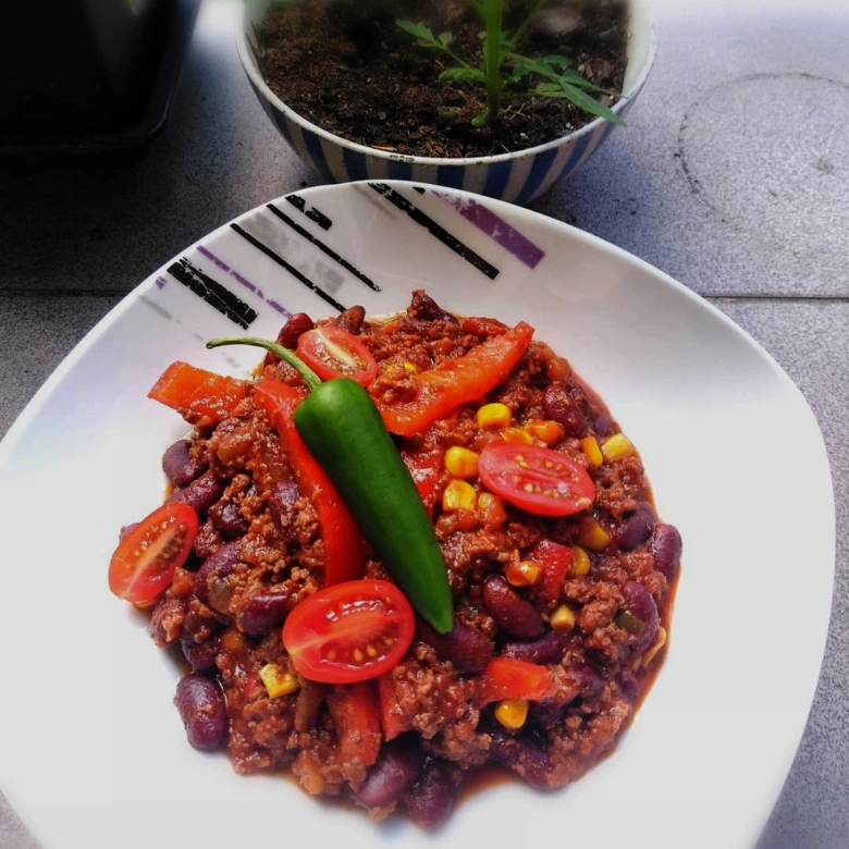 Položka chilli con carne s rajčaty na bílé talíři.