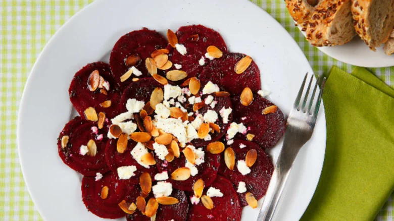 Carpaccio z červené řepy s mandlemi a syrem na talíři.