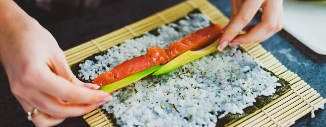 Ruční příprava rýžového sushí rolky se lososem.