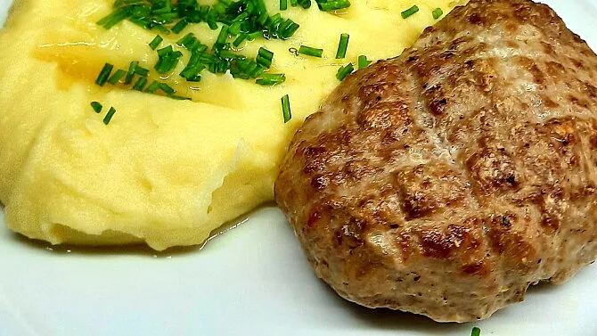 Připravený máslový řízek s bramborovou kaší na bílém talíři.