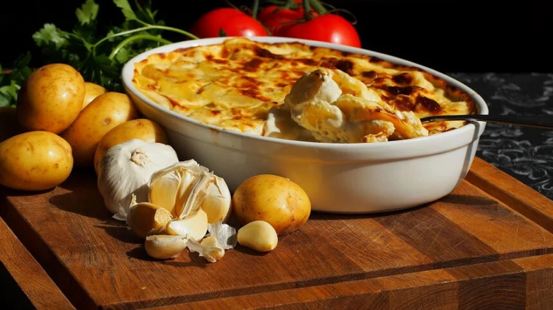 Gratinované brambory v keramické misce s česnekem a rajčaty.