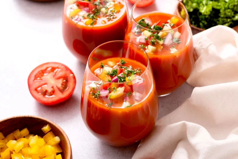 Tři sklenice s červenou polévkou gazpacho ozdobené zeleninou.