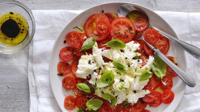 Caprese salát s rajčaty, mozzarellou a bazalkou na talíři.