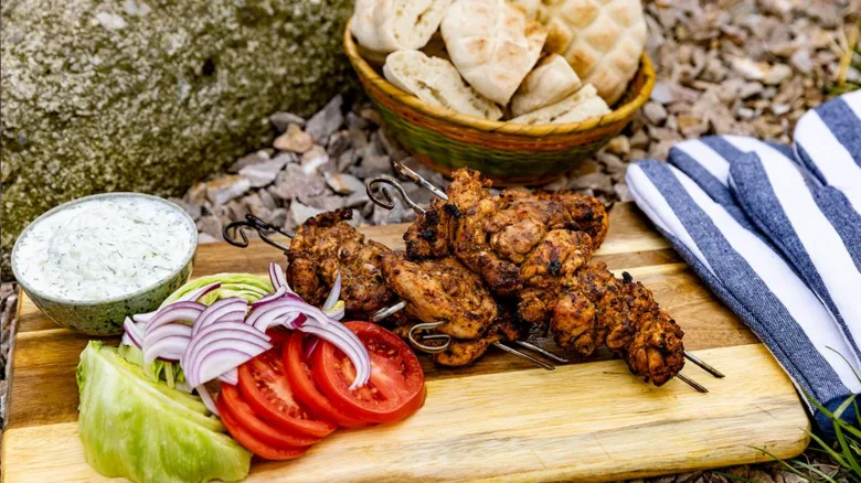 Pečené kuřecí špejle souvlaki s čerstvou zeleninou a jogurtovou omáčkou.