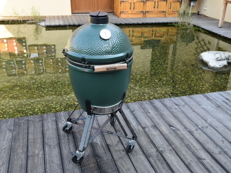 Zelený keramický gril na dřevěné terase připravený k pečení vepřové panenky.