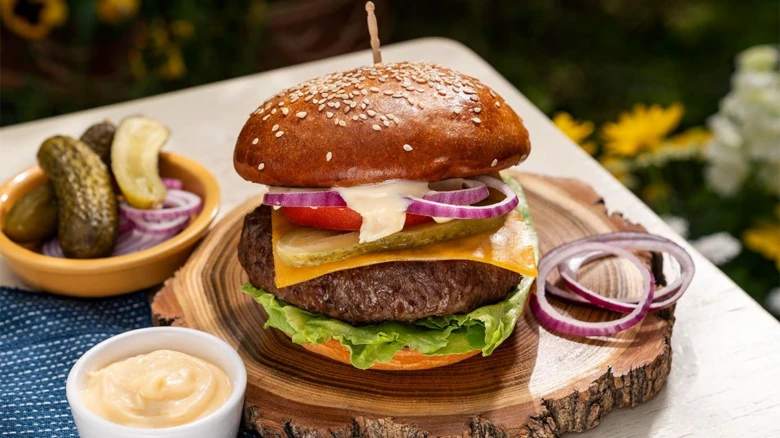 Domácí hovězí hamburger s sýrem, okurkou a cibulí na dřevěném podstavci.