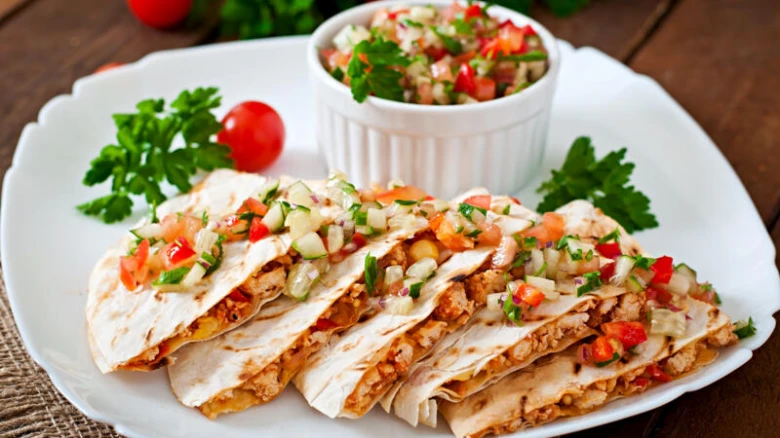 Použité kuřecí quesadilly s čerstvou omáčkou na bílém talíři.