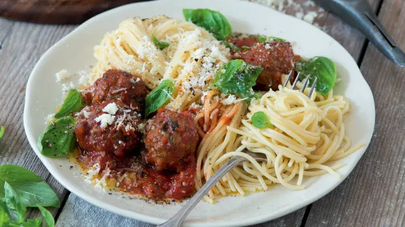 Pasta s masovými kuličkami v rajčatové omáčce na talíři.