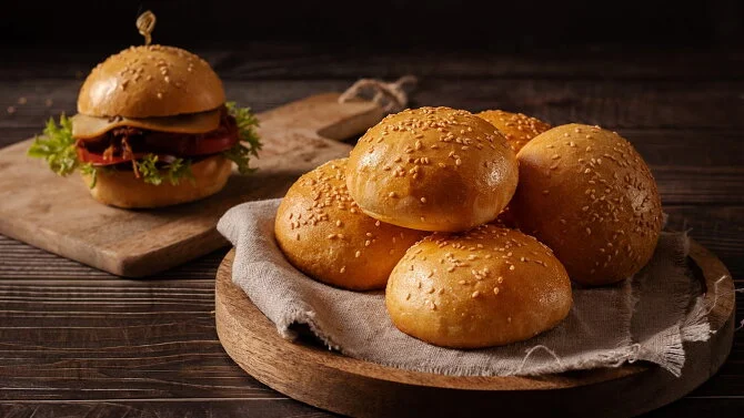 Zlaté hamburgerské housky s sezamem na dřevěném podnosu.