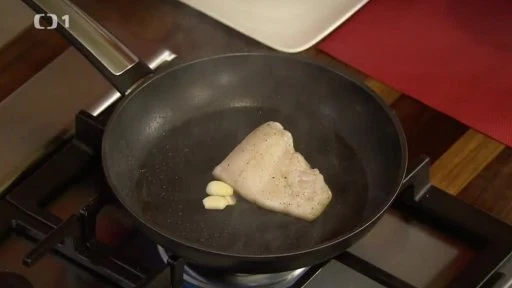 Bílá ryba se smaží na pánvi s česnekem.