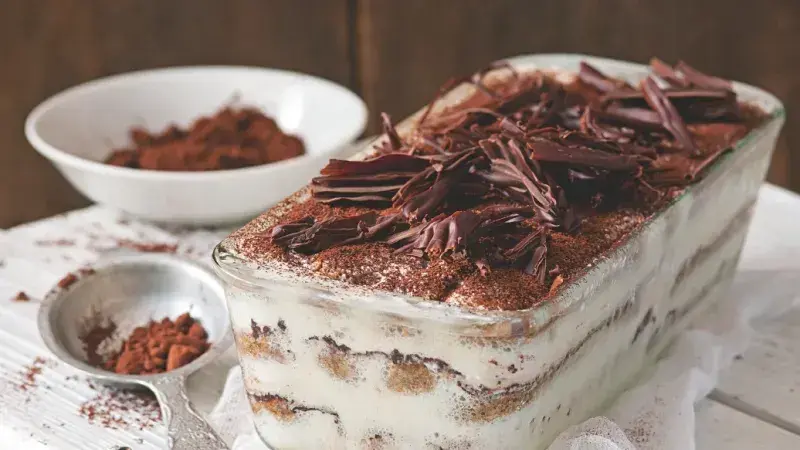 Tiramisu s čokoládovými lupínky a kakaem v skleněné mísce.