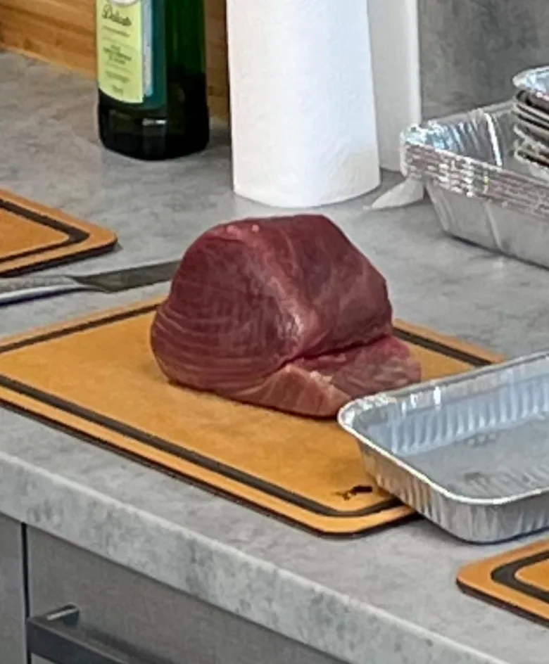 Surový tuňák na dřevěném prknu připravený k vaření.