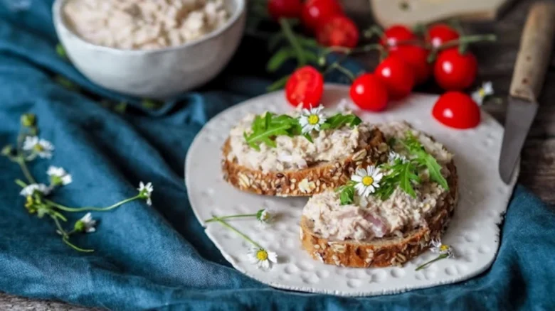 Dva plátky chleba s tuňákovou pomazánkou, vejci a majonézou ozdobené zeleninou.