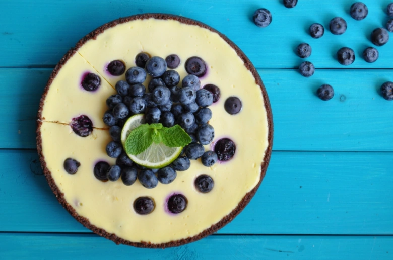 celý borůvkový cheesecake s čerstvými borůvkami na modrém dřevěném povrchu