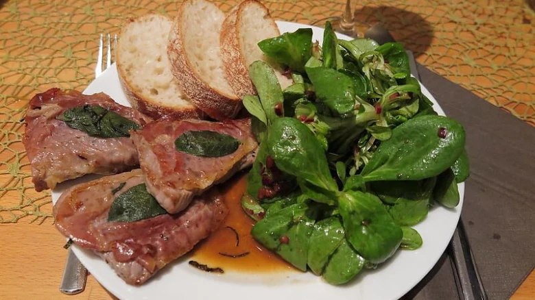 Telecí saltimbocca se šalátom a kousky chleba na talíři.