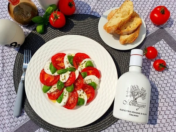 Caprese salát s rajčaty, mozzarellou a bazalkou na bílém talíři.
