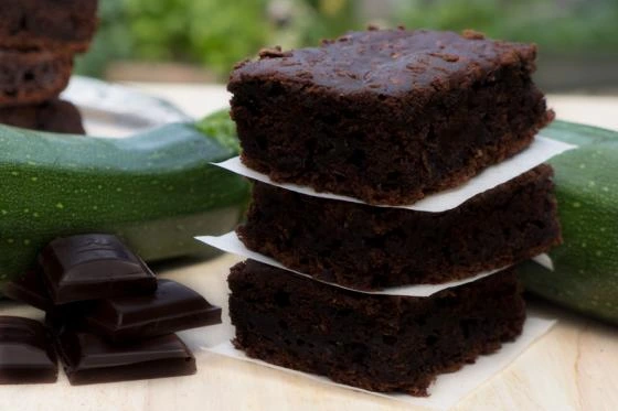Hromada čokoládových brownies vedle cukety na dřevěném povrchu.