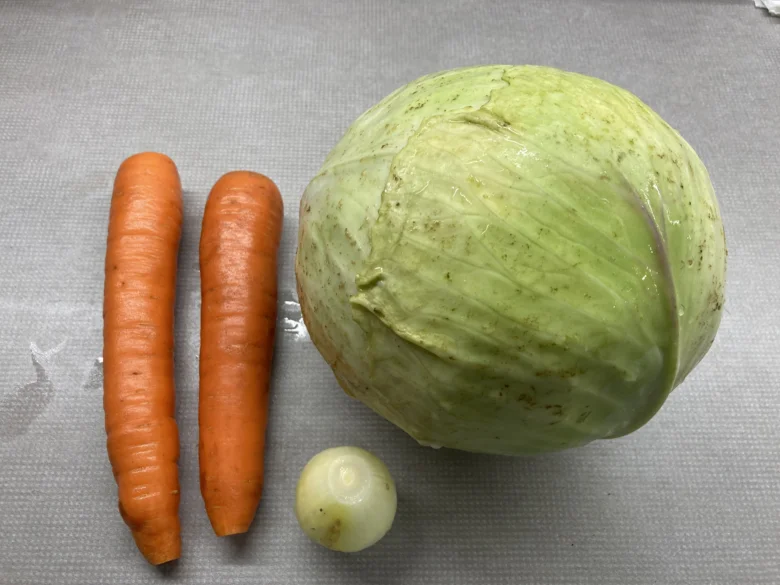 Zelenina pro coleslaw: zelí mrkev a cibule na šedém podkladu.