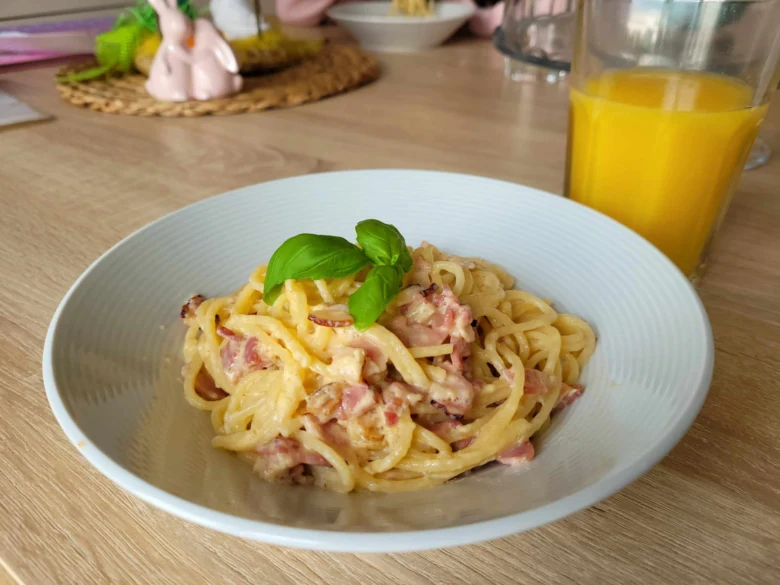 Bílá miska s krémovými špagetami karbonará se slaninou a bazalkou.