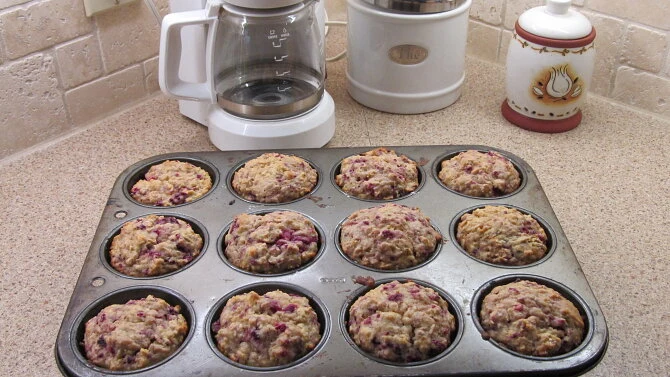 Zpečené ovesné muffiny s ovocem v plechu na kuchyňské desce.