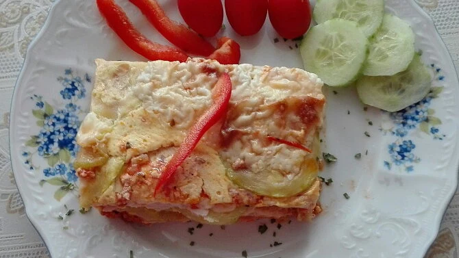 Kousek cuketové lasagne s paprikou a okurkou na talíři.