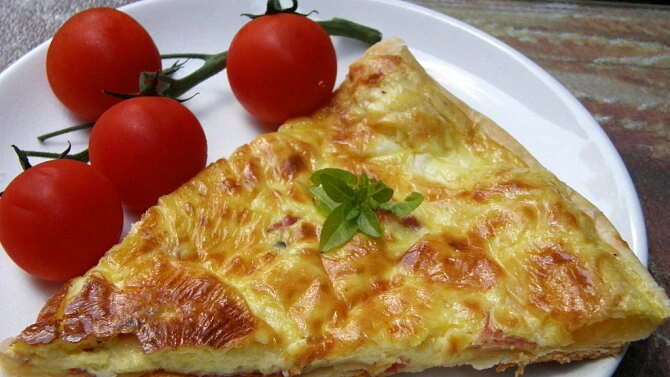 Kousek slaného koláče s rajčaty na bílém talíři.