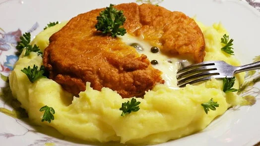 Zlatě opečená kotleta z masa na bramborové kaši s kořením.