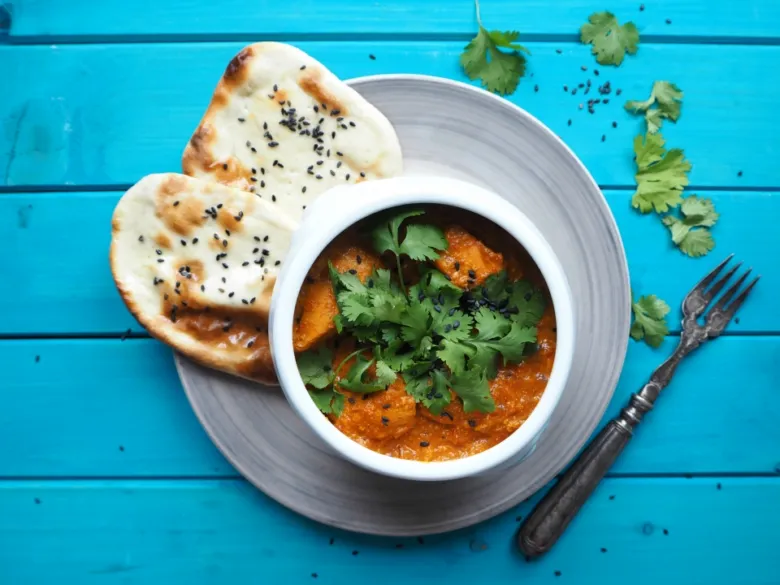 Mísa kuřecí tikka masala s chutnou omáčkou, koriandrem a dvěma kousky nánu.