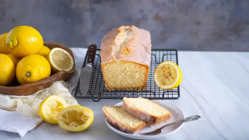 Citronová bábetu s glazurou na mřížce vedle čerstvých citronů.