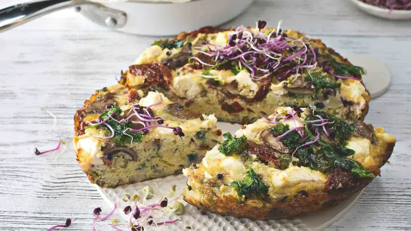 Skládaný frittata s špenátem, houbami a syrem na bílém talíři.