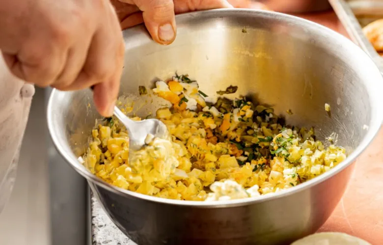 Ruce míchají ingredience pro vaječnou pomazánku ve stříbrné misce.