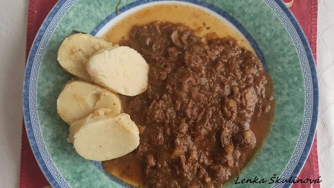 Příprava dančího guláše s knedlíky na talíři.