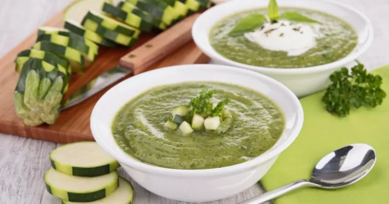 Dva misky zelené krémové polévky ze cukety s ozdobou.