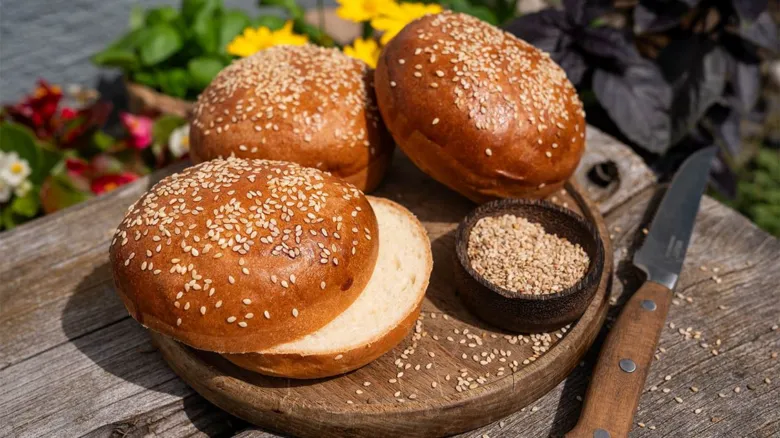 Zlaté hamburgerské housky s sezamem na dřevěném talíři.