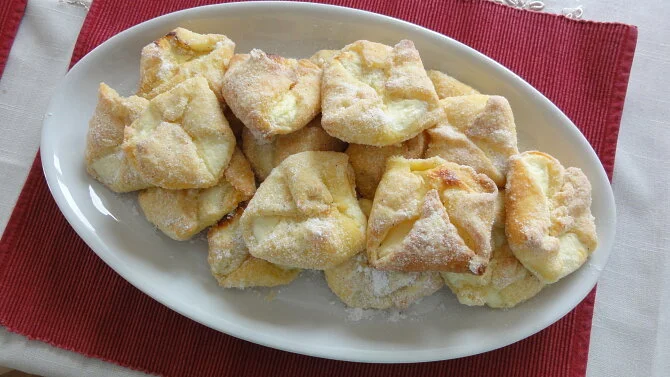 Tvarohové šátečky posypané cukrem na bílém talíři.