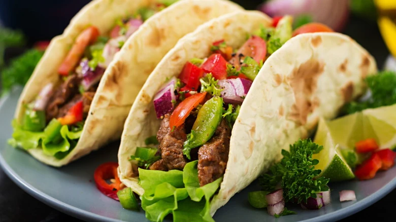 Tři mexické taco s morkovím, zeleninou a masem na talíři.