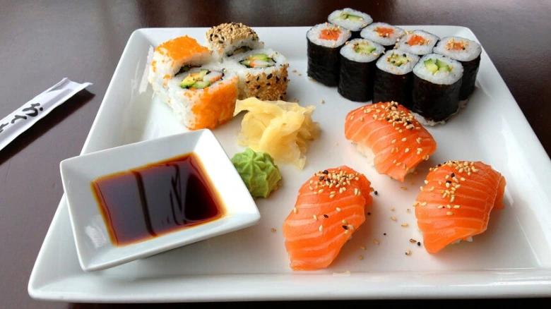 Bílá deska s různými druhy sushi, lososem a omáčkou.