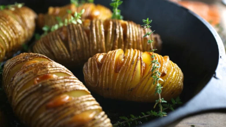 Zlaté pečené brambory Hasselback s čerstvou bylinkou v pánvi.