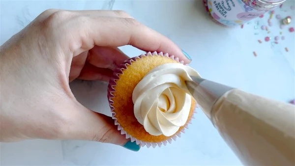 Ruka natáčí máslový krém na špičku muffinu.