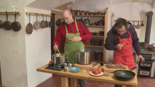 Dva muži vaří polévku v kuchyni s hrncemi na stole.