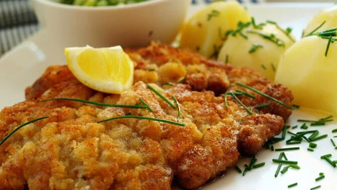 Zlatě opečený vídeňský řízek s bramborami, citronem a jehličím.