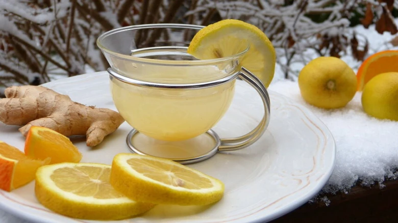 Sklenička zázvorového čaje s citronem na sněhu se surovými ingrediencemi.