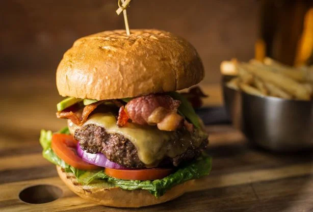 Hovězí hamburger s bryndzou, slaninou a zeleninou na dřevěném talíři.