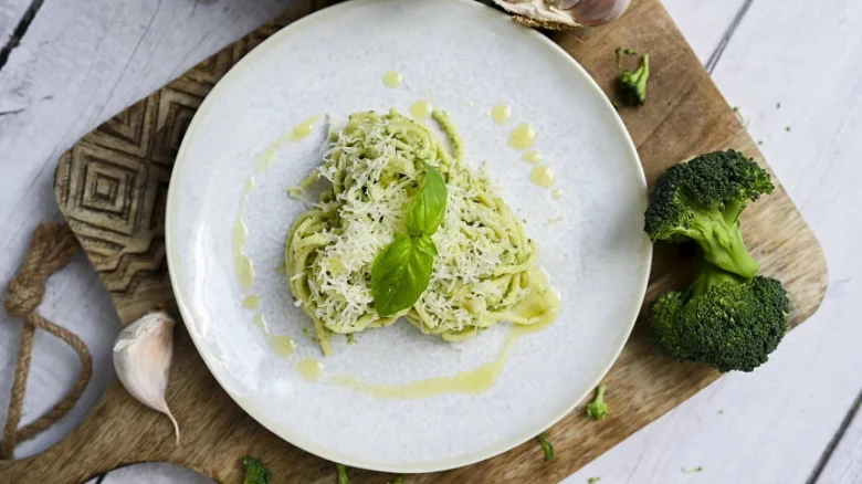 Taler s těstovinami v pesto se bazalkou na dřevěném prknu.