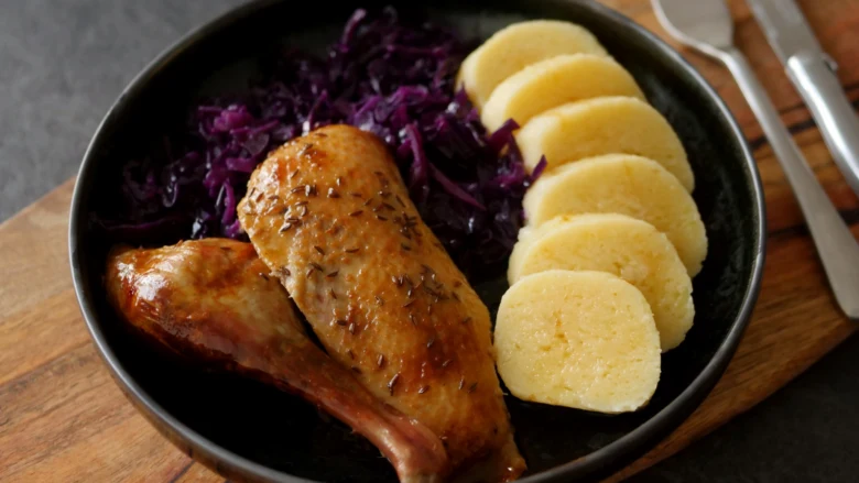 Pečená kachna s červenou kapustou a knedlíkem na talíři.