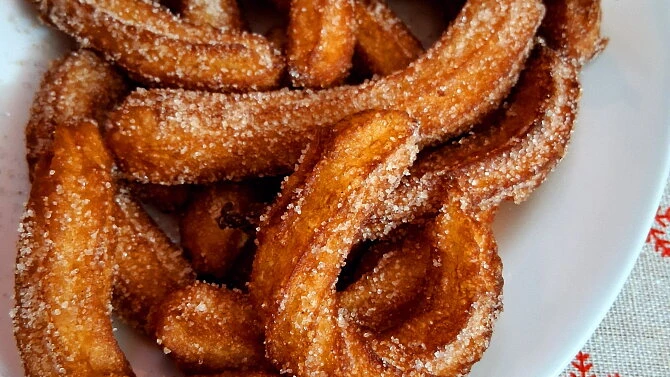 Zlatohnědé churros posypané cukrem s kořením na bílém talíři.