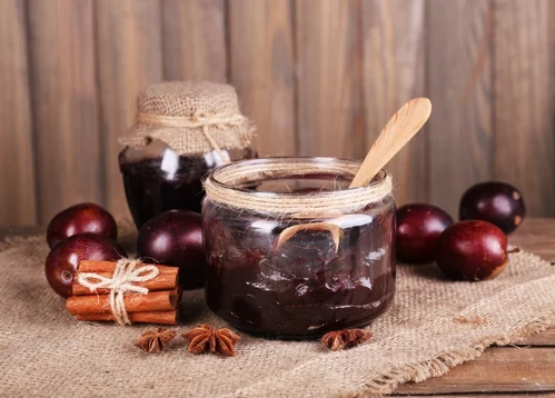 Skořicové tyčinky a hřebíček kolem sklenice švestkové klevely
