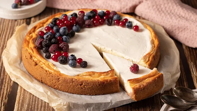 Tvarohový cheesek s ovocem na dřevěném podkladu.