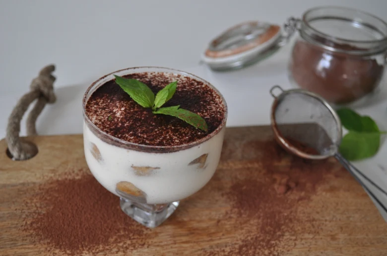 Tiramisu v sklenici posypaný kakaem s máty na dřevěném podkladu.